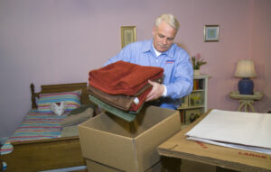 Arpin of RI packer standing in a bed room packing towels into a 3 cube carton