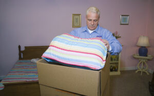Arpin of RI packer standing in a teenager's bed room carefully packing linens and beddings into a 6 cube box