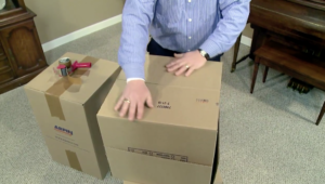 Arpin of RI packer standing in a dining room carefully folding in the second two bottom flaps of a carton