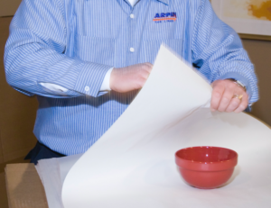 Arpin of RI packer in a dining room carefully wrapping a china bowl in paper