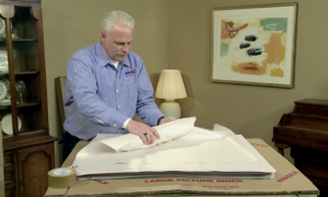 Arpin of RI packer in a dining room wrapping a fragile glass in white newspaper on a properly constructed wrapping station