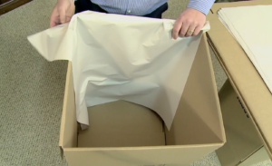 a large carton getting lined with sheets of white news paper.
