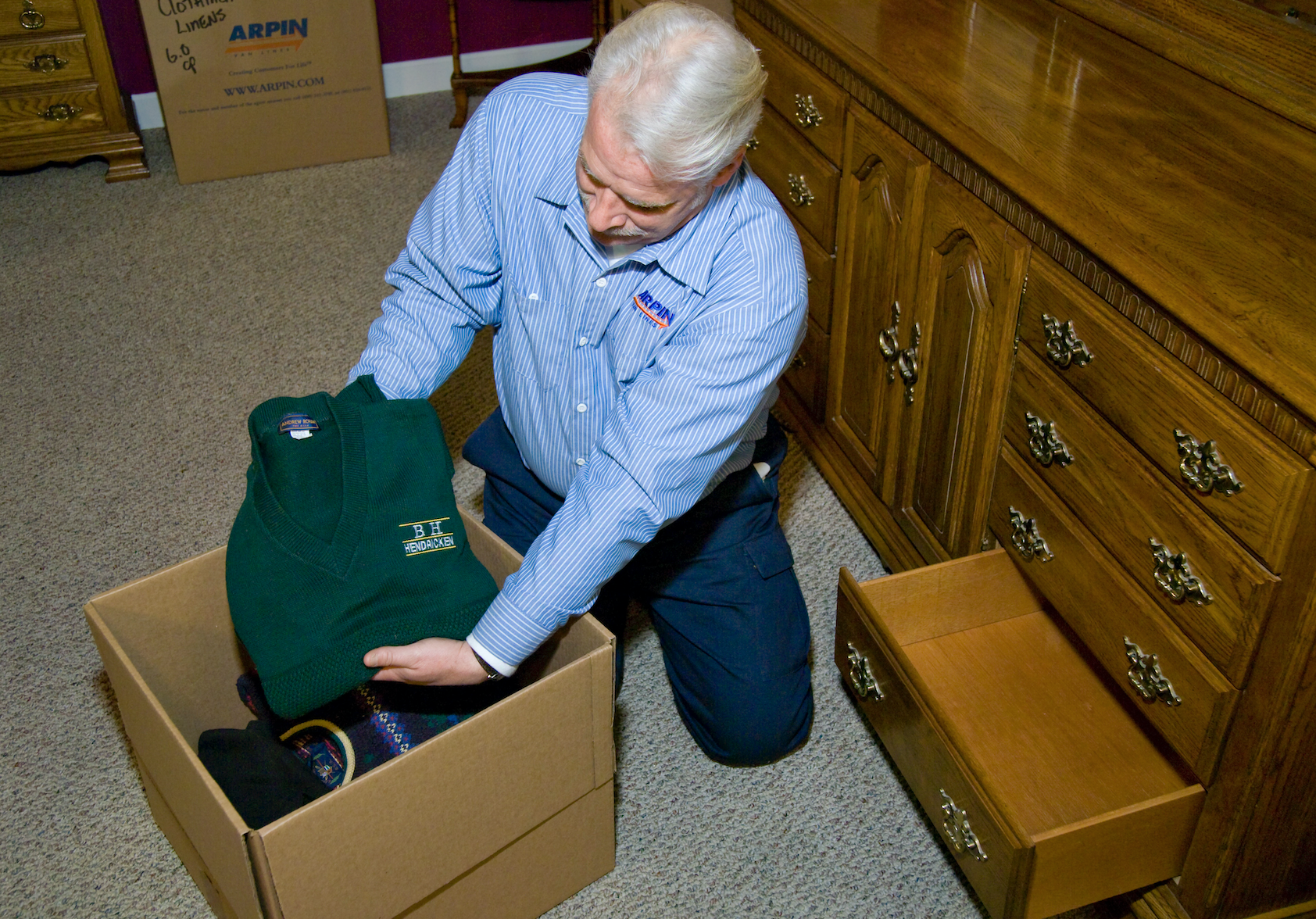 Arpin of RI packer in a bed room removing folded sweaters from a drawer and packing them in a carton.