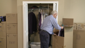 Arpin of RI packer in a bed room packing clothing into a wardrobe carton.