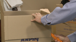 Arpin of RI packer in a bed room cutting a front flap for a baby wardrobe carton.